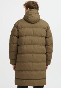 Olive green puffer coat, mid-thigh length, quilted design with horizontal stripes, a hood, and elastic cuffs. Textured, warm, and insulated.