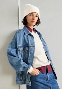 Denim jaka ar pārāk lielu piegriezumu, gaiši zila krāsa un pogu aizdare. Uzvilkta pāri baltam džemperim un tumši sarkanai kreklam ar apkakli.