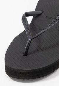 Mustat flip-flopit, joissa on teksturoitu kumipohja, tyylikkäät kumihihnat ja klassinen muotoilu, jossa on hieman kohotettu korko.