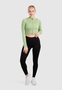Ljusgrön kortad zip-up jacka med ribbat mönster, tillsammans med högmidjade svarta leggings och vita träningsskor.