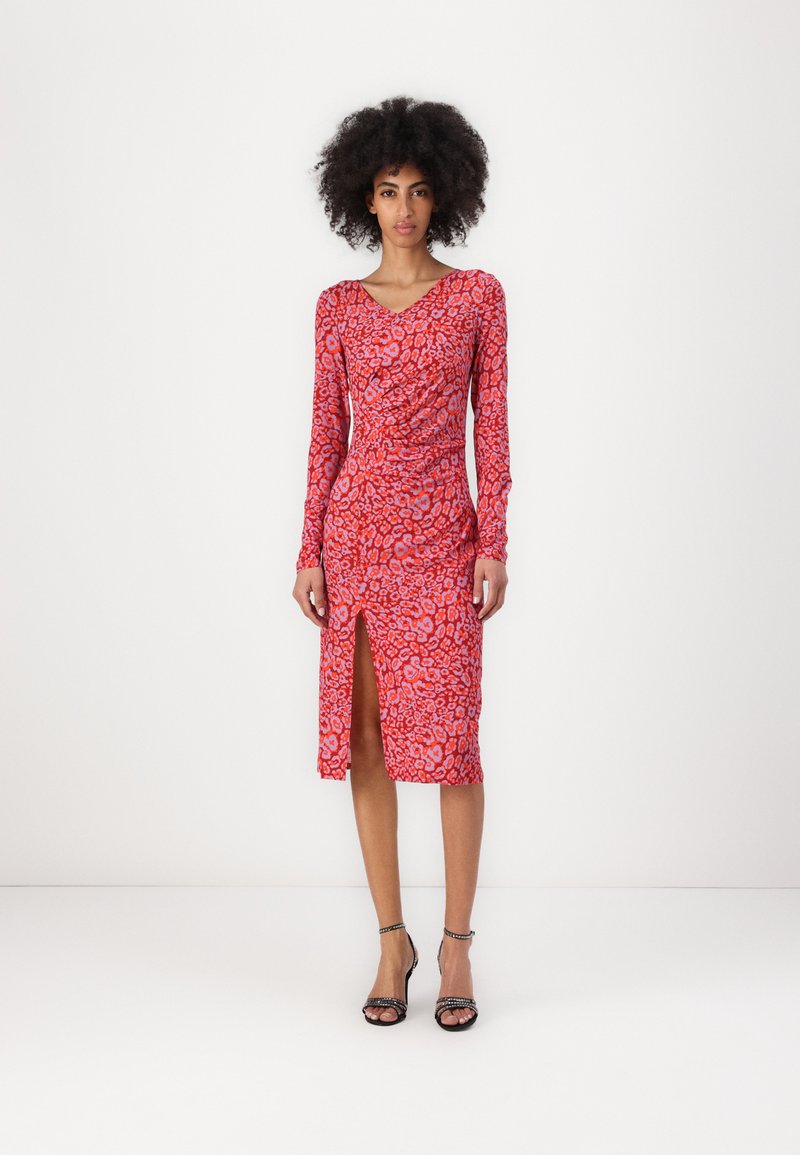 Rotes Langarmkleid mit Leopardenmuster, das ein Wickeldesign und einen Oberschenkel-hohen Schlitz aufweist. Kombiniert mit schwarzen Riemchen-Heels.