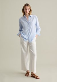 Helles blaues Button-Down-Shirt, weiße weite Hose und braune Sandalen mit Riemchen. Strukturiertes Material und lockere Passform verleihen ein lässiges Erscheinungsbild.