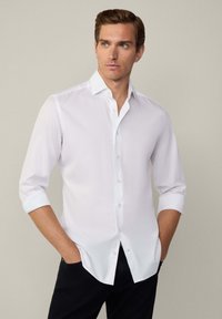 Witte overhemd met lange mouwen opgerold tot de ellebogen. Glad materiaal, klassieke kraag en een rechte zoom. Zwarte broek.
