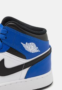 Tenisky Air Jordan s čiernym, modrým a bielym koženým zvrškom, s textúrovaným čiernym golierom a logom Air Jordan na boku.