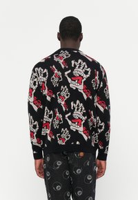 Zwarte trui met een gedurfde, kleurrijke grafische print van schreeuwende gezichten en handen in rood, wit en grijs, gebreide textuur.