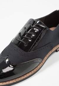 Schwarze Lackleder- und marineblaue Canvas-Schnürschuhe mit durchbrochener Gestaltung, runder Zehenpartie und beigem gesticktem Sohlenrand.