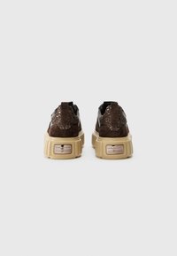 Baskets compensées en suède marron avec des accents noirs scintillants, un dos texturé, des semelles épaises beiges et un logo métallique sur le talon.