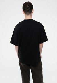 Black cotton t-shirt featuring a loose fit, short sleeves, and a rounded neckline. The fabric appears soft with a smooth texture.