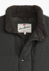 Mörkgrå vadderad jacka med fleece-fodrad krage, märkesetikett, metalldragkedja och tryckknappsstängning. Har ett slätt, strukturerat material.