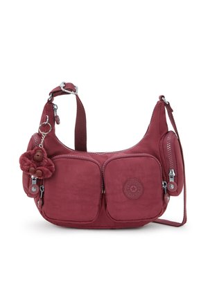 Small maroon shoulder bag with two front pockets, side zip compartments, adjustable strap, and a plush monkey keychain attached.