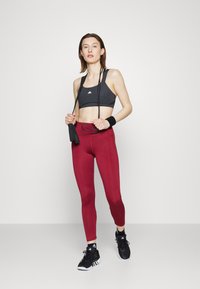 Top desportivo preto, leggings bordeaux de cintura alta, sapatos de desporto pretos. A modelo segura uma corda de saltar, usando faixas de suor nos pulsos, design minimalista.