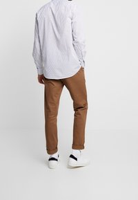 Witte button-up shirt met kleine marineblauwe stippen, beige chino's en witte sneakers. Het shirt heeft een ronde onderrand en lange mouwen.