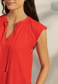 Rode lichte blouse met een ronde halslijn, korte capmouwen en een sluiting met strikjes; heeft een subtiele textuur en een losse pasvorm.