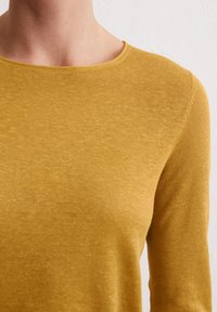 Senfgelbes Langarmshirt mit rundem Ausschnitt und weichem, strukturiertem Stoff. Die Nähte sind dezent und gut verarbeitet.
