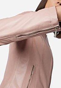 Ljusrosa läderjacka med en figursydd design, dragkedjedetaljer på ärmarna och en slät textur med subtila sömnadsdetaljer.