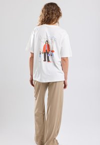 White cotton t-shirt with a colorful graphic on the back, featuring a figure in an orange jacket and black pants. Loose fit.