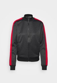 Svart zip-up jacka med ett subtilt logomönster, röda sidostråk, ribbad krage, ärmar och nederkant. Tillverkad av mjukt, lättviktigt tyg.