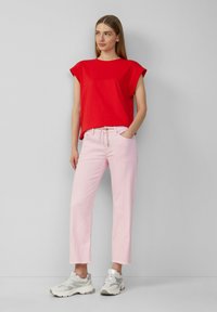 Top rosso a maniche corte abbinato a jeans cropped rosa chiaro e sneakers grigie. I jeans hanno un cordoncino in vita e orlo sfrangiato.