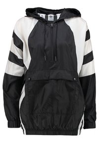 Svart och vit huva vindjacka med framficka, med djärva diagonala ränder, elastiska manschetter och ett lätt, texturerat tyg.