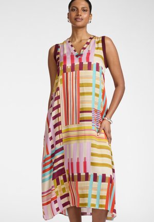 Vrouw draagt een kleurrijke mouwloze midi-jurk met geometrische verticale en horizontale strepen in rood, geel, paars, blauw en beige.