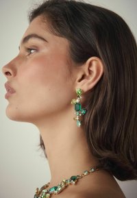 Grüne und blaue Edelsteinohrringe zeigen verschiedene Formen und Größen, gefasst in goldfarbener Hardware, ergänzt durch eine passende Halskette.