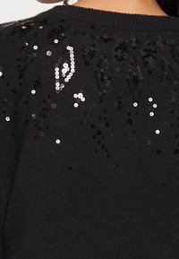 Czarny sweter z dzianiny z fakturowanym wzorem zdobionym cekinami i koralikami na górnej części pleców. Okrągły dekolt z prążkowanym obszyciem.