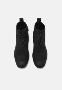 Sorte ankelboots laget av semsket skinn, med en jevn tåhette, kontrasterende matte og teksturerte overflater, med snøring og glidelås på siden.
