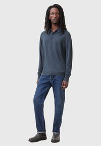 Mørkeblå langærmet polo skjorte med krave, struktureret stof og lille logo på brystet, parret med blå denim jeans og sorte støvler.