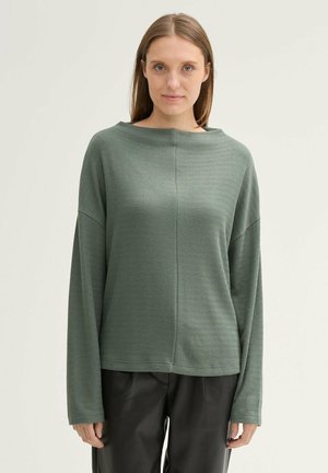 Groene lange mouwen top met een brede bootnek, textuur ribstof, relaxte pasvorm en verlaagde schouders, gecombineerd met zwarte broek.