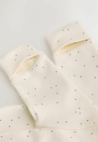 Cream-colored fabric with small black scattered dots and folded cuffs, likely soft clothing or textile material.