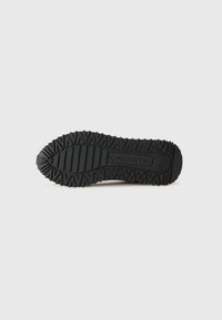 Black rubber shoe sole featuring a zigzag tread pattern and textured surface, with branding engraved near the center.