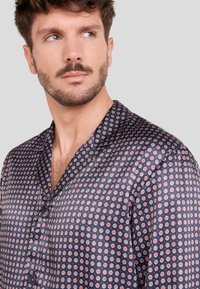 Camisa navy de botonadura en tejido suave con un patrón circular repetido en rojo y blanco, que presenta un cuello con muesca y mangas cortas.