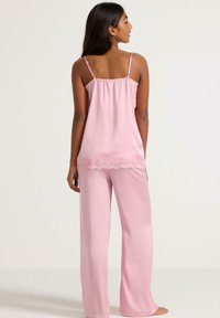 Pink satin pajama set featuring a cami top with adjustable straps and a lace trim, paired with long, loose-fitting pants. Smooth texture.