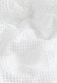 Tissu en crochet blanc avec des motifs géométriques et des trous texturés, délicatement plié pour montrer la profondeur et les détails.