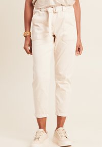 Lichtbeige high-waisted broek met een ceintuur in de taille, zijzakken, opgerolde manchetten en een gladde katoenen textuur. Gecombineerd met lichte sneakers.