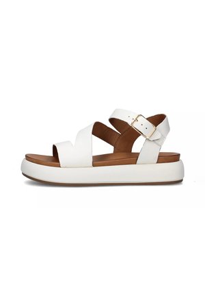 Sandalias de cuero blancas con un diseño de tiras cruzadas, cierre de hebilla y una suela gruesa blanca con una plantilla marrón acolchada.