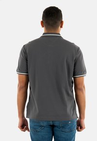 Camisa polo gris con cuello y ribete blanco en las mangas. Diseño sencillo, de mangas cortas y textura de tela suave. Jeans visibles por debajo.