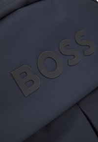 Navy blue backpack featuring a textured fabric, with bold black "BOSS" logo prominently positioned on the front.