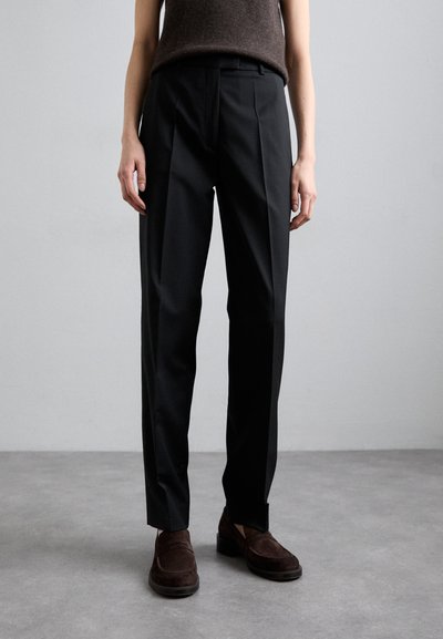 Pantaloni negri, croiți pe corp, cu un fit drept, având pliseuri în față și o textură netedă. Asortați cu pantofi slip-on din suede maro închis.