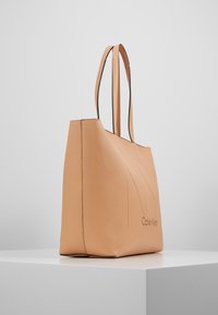 Kabelka Calvin Klein z jemného broskvového kůže, strukturovaný tvar, dvojité ramenní popruhy, embosované logo a jemné detaily šití.