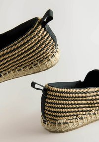 Espadryle z czarną płócienną cholewką i plecionym beżowo-czarnym detalem tekstylnym. Posiadają podeszwę z jutowego sznura oraz tylną pętelkę z tkaniny ułatwiającą zakładanie.