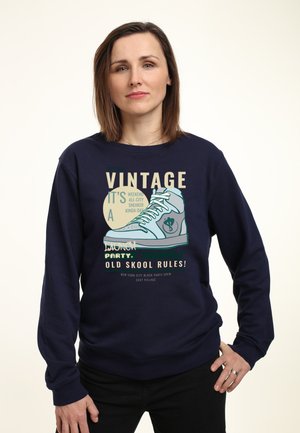 Felpa navy con una grafica di sneaker retrò. Presenta il testo "Vintage," "Launch Party," e "Old Skool Rules!" in vari colori e caratteri.