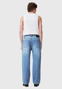 Jeans decolorate, în nuanță albastru deschis, cu talie înaltă și croială lejeră, având cinci buzunare. Sunt asociate cu un top alb fără mâneci, cu textură canelată.