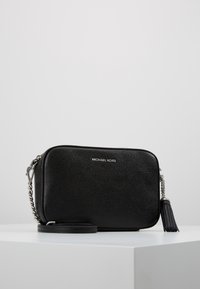 Schwarze Leder-Crossbody-Tasche mit strukturierten Oberflächen, silberner Hardware, abnehmbarem Trageriemen und einem Quastenakzent. Markenlogo auf der Vorderseite.