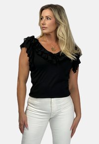 Czarny top bez rękawów z falbaniastym dekoltem, dopasowany fason, wykonany z miękkiego materiału. W zestawieniu z białymi dżinsami, tworzy kontrastowy wygląd.
