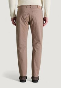 Pantalones de algodón beige con corte recto, que cuentan con dos bolsillos traseros y trabillas para cinturón. Llevados con calzado gris, vista desde atrás.