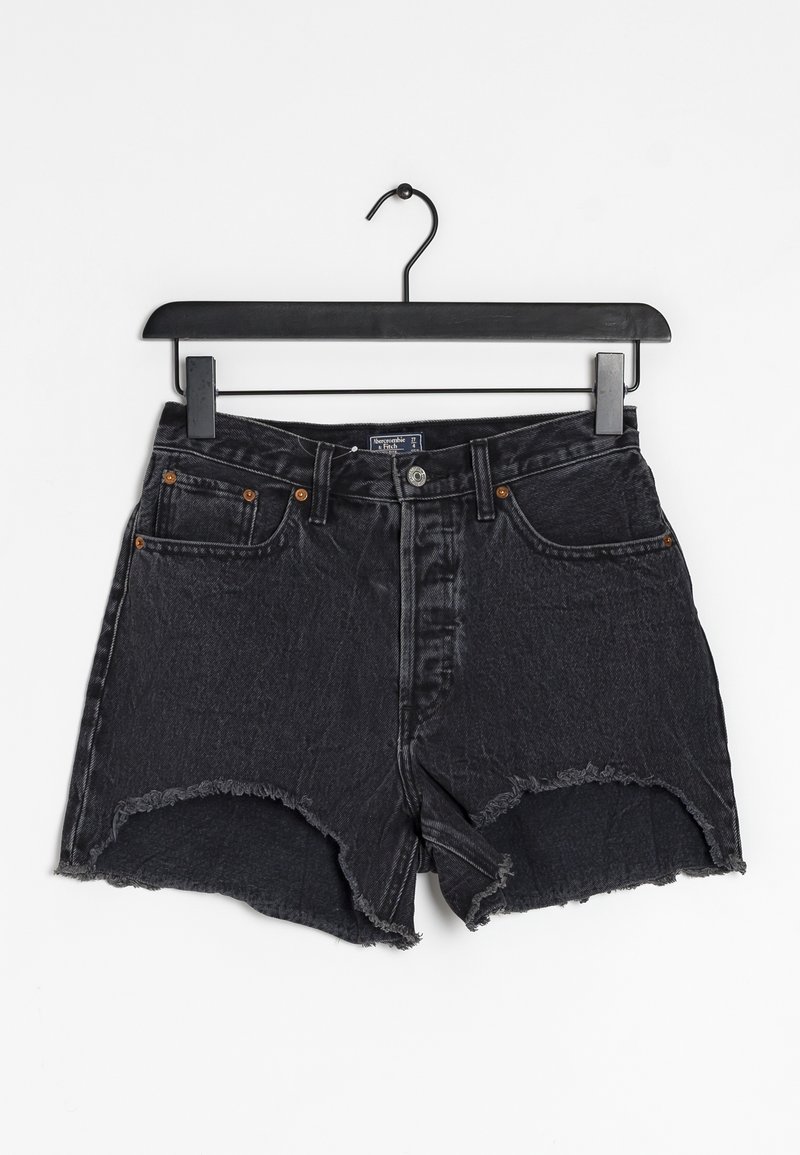 Schwarze Jeansshorts, die an einem Kleiderbügel hängen. Besitzen einen ausgefransten Saum, fünf Taschen und kupferfarbene Hardware-Details.