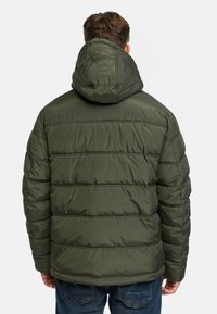 Gewatteerde jas in donkergroen met een capuchon, voorzien van horizontale naden en een gladde textuur. Ontworpen voor warmte en isolatie.