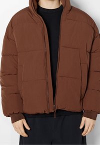 Giacca imbottita marrone con cappuccio, dotata di zip frontale, tasche laterali e polsini a costine, realizzata in un materiale liscio e leggero.
