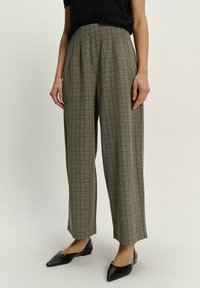 Checked, high-waisted trousers in beige and brown, featuring a loose fit, pleats, and straight legs. Worn with black pointed flats.